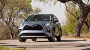 A silver 2021 Toyota Highlander Platinum AWD midsize SUV parked on a narrow road overgrown with trees and grass