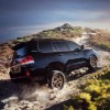 A black 2021 Toyota Land Cruiser four-wheel-drive full-size SUV travels on a dusty, rocky path up a hill