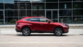 A red 2021 Toyota Venza LE midsize crossover SUV parked on brick pavers next to a sidewalk outside a glass building