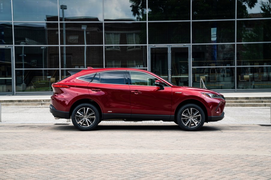 A red 2021 Toyota Venza LE midsize crossover SUV parked on brick pavers next to a sidewalk outside a glass building