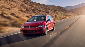 A red 2021 Volkswagen GTI four-door hatchback traveling on a two-lane highway through arid mountains on a sunny day