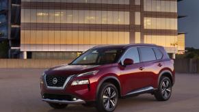 A red Nissan Rogue parked in front of a glass-front administrative building