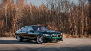 A dark-green 2022 BMW Alpina B8 Gran Coupe parked by a winter-time forest