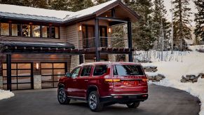 The rear 3/4 view of a red 2022 Jeep Wagoneer Series II next to a wooden cabin in a snowy forest