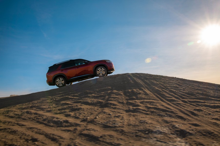 A red 2022 Nissan Pathfinder driving up a sand dune