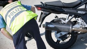 A German police officer in a high-vis jacket checks how loud a black motorcycle's exhaust pipe is