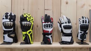 A selection of gauntlet-style motorcycle gloves on display on a wooden stand