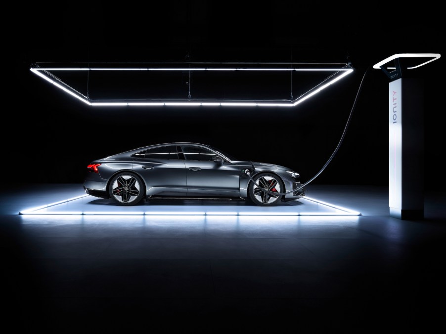 A dark metallic Audi e-tron GT electric four-door car parked under lights in a dark room