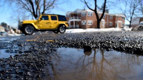 A Jeep Wrangler avoids hitting a pothole on a street.