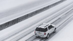 A white Ford Expedition SUV travels on a snowy highway.