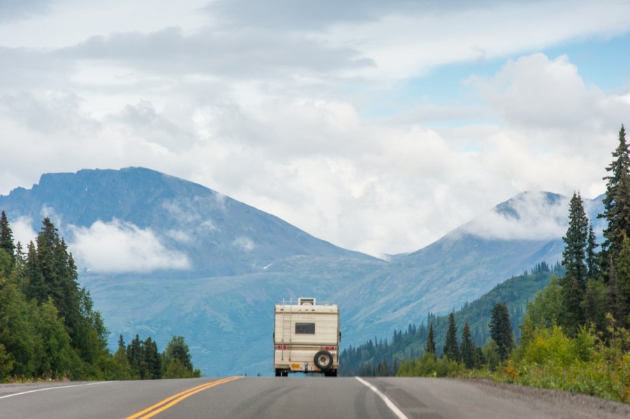 An RV drives down the road with mountains in the background