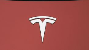 A silver Tesla logo on a red vehicle hood