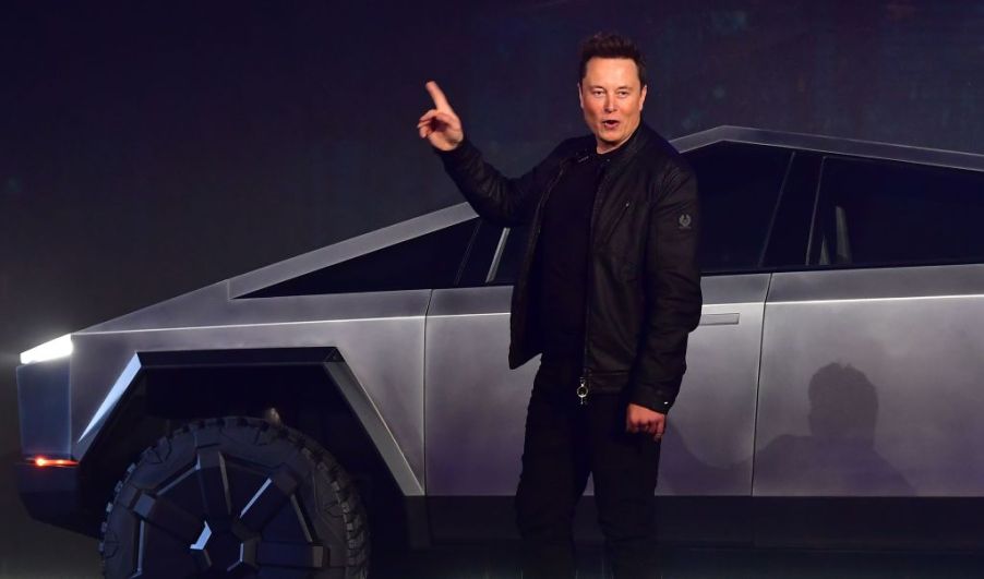 Tesla CEO Elon Musk points upward as he stands in front of a stainless steel Cybertruck