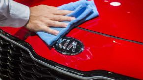 A man wipes down the front end of a red kia sportage