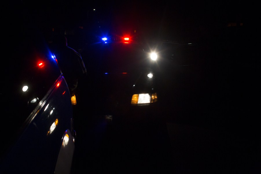 A police car with red and blue lights behind a motorist's vehicle during a traffic stop at night