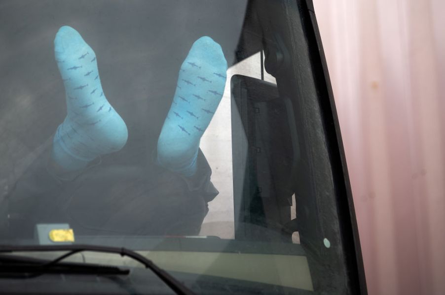 A trucker driver rests his feet on the dashboard as he rests