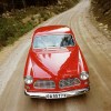 A red 1961 Volvo Amazon drives down a dirt road