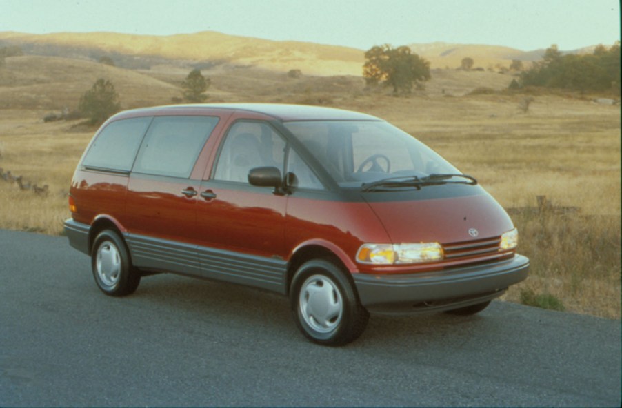 A red 1991 Toyota Previa minivan parked on a rural road with hills in the background