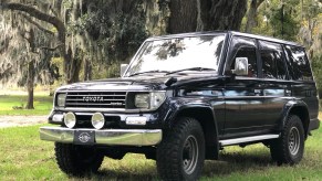 A black 1993 Toyota Land Cruiser Prado on a lawn next to a tree