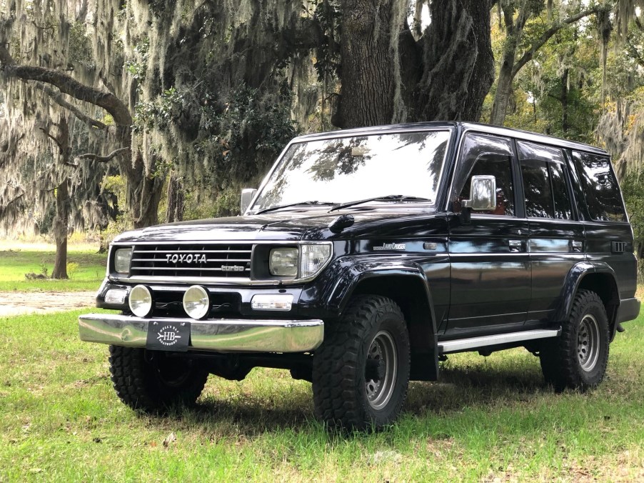 A black 1993 Toyota Land Cruiser Prado on a lawn next to a tree