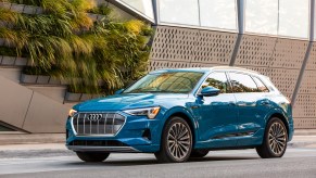 A bright-blue 2019 Audi e-tron electric crossover SUV parked on a street outside a modern building