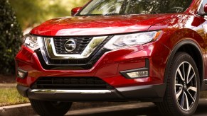 A red metallic 2019 Nissan Rogue compact crossover SUV parked next to a curb