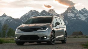 A silver 2020 Chrysler Pacifica Limited minivan parked on gravel in front of snowcapped mountain with the sun behind them