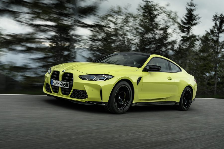 A yellow-green 2021 BMW M4 Competition driving on a forest-lined road