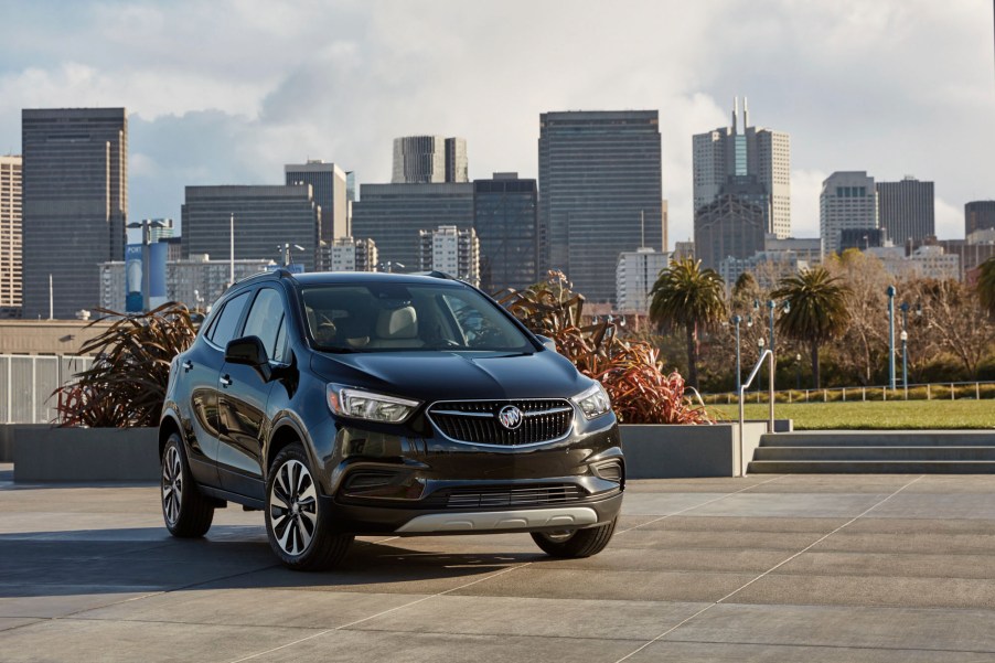 A dark-colored 2021 Buick Encore luxury subcompact SUV parked in front of a city skyline