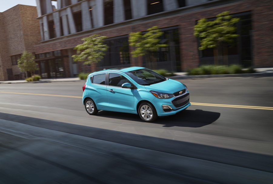 A blue Chevy Spark driving down a downtown street