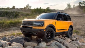 An orange metallic 2021 Ford Bronco Sport compact crossover SUV parked on rocks beside a dirt road