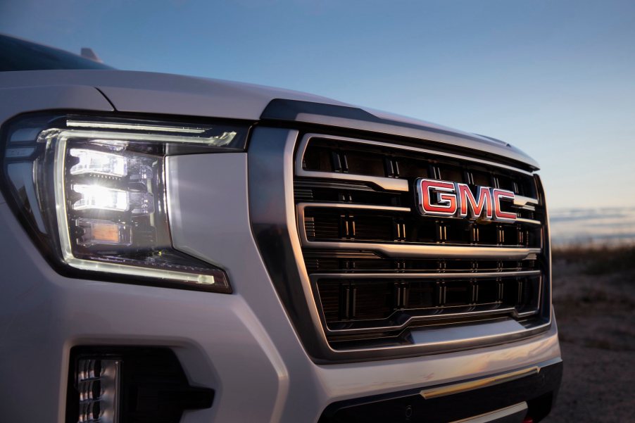 The right front headlight and grille of a pearl-white 2021 GMC Yukon AT4 full-size SUV