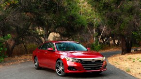 A red 2021 Honda Accord Hybrid sedan parked on a narrow road surrounded by green bushy trees