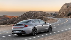 A silver 2021 Hyundai Sonata N Line midsize sedan on a curvy two-lane mountain highway overlooking an ocean