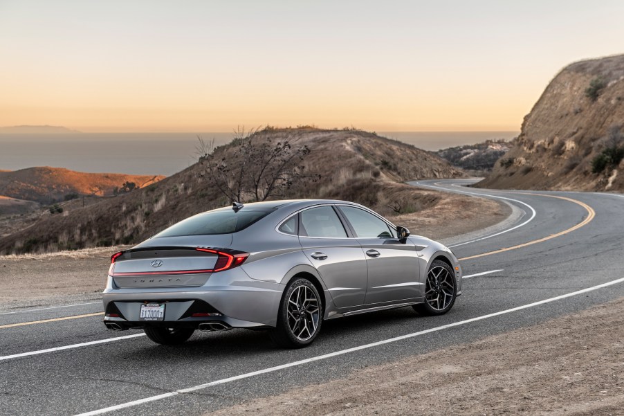 A silver 2021 Hyundai Sonata N Line midsize sedan on a curvy two-lane mountain highway overlooking an ocean