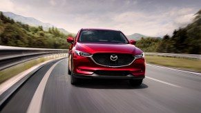 A front view of a red 2021 Mazda CX-5 compact crossover SUV traveling on a two-lane highway through the mountains