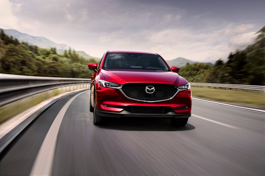 A front view of a red 2021 Mazda CX-5 compact crossover SUV traveling on a two-lane highway through the mountains