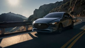 A dark-colored 2021 Mazda3 2.5 Turbo hatchback traveling on a two-lane mountain highway on a sunny day