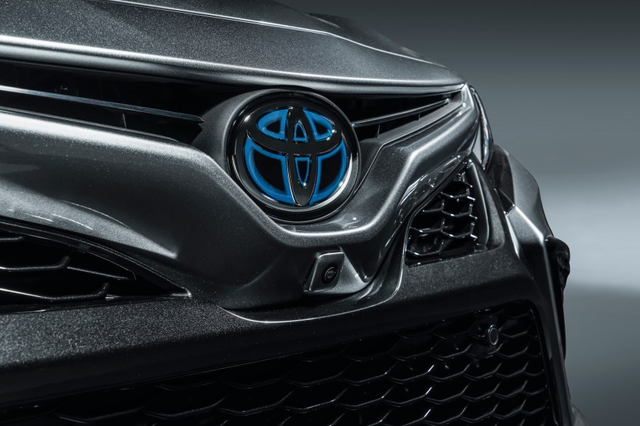 A dark-gray metallic 2021 Toyota Camry Hybrid sedan's honeycomb grille bears a silver and blue Toyota logo