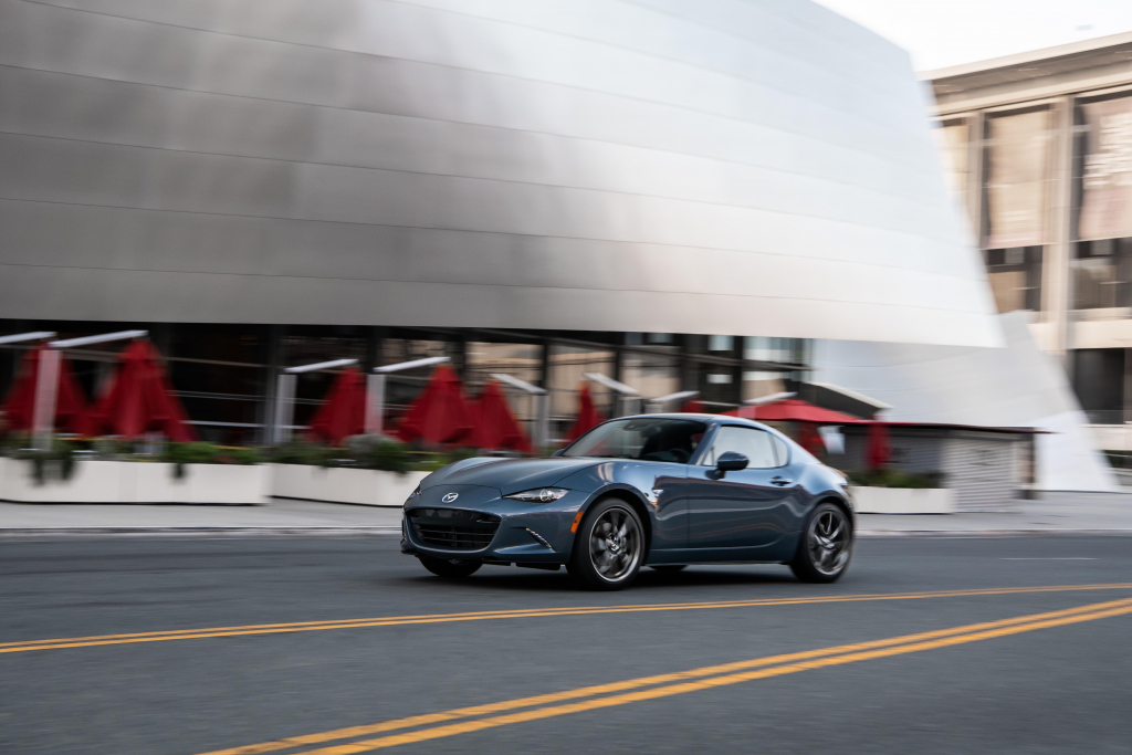 A muted blue 2021 mazda mx-5 miata driving through the city