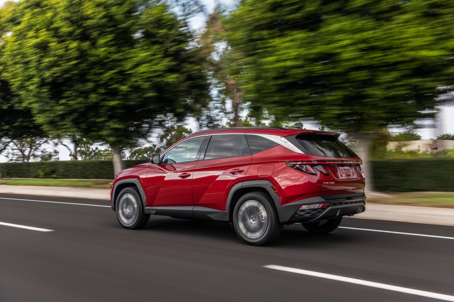 A red 2022 Hyundai Tucson travels on a highway lined with trees, grass, and a hedge