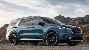 A blue 2022 Kia Carnival parked by some desert mountains