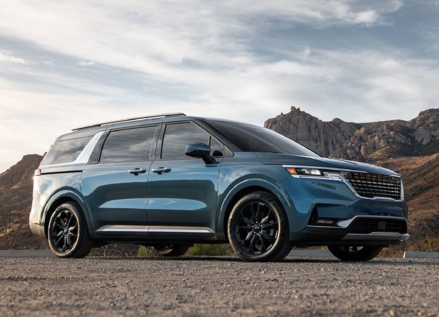 A blue 2022 Kia Carnival parked by some desert mountains