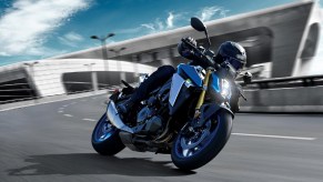 A black-clad rider taking a blue-and-silver 2022 Suzuki GSX-S1000 around a highway corner