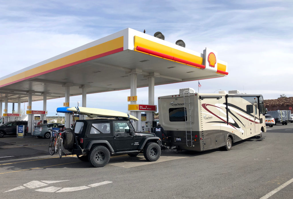 an RV towing a Jeep Wrangler fueling up at a shell station