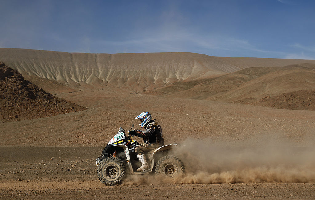 an ATV rider on a Can-Am at the Dakar Rally riding through a vast desert