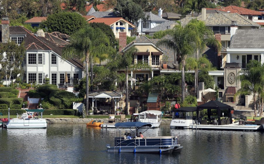 An electric-powered pontoon boat skims across Lake Mission Viejo, past the homes and private docks