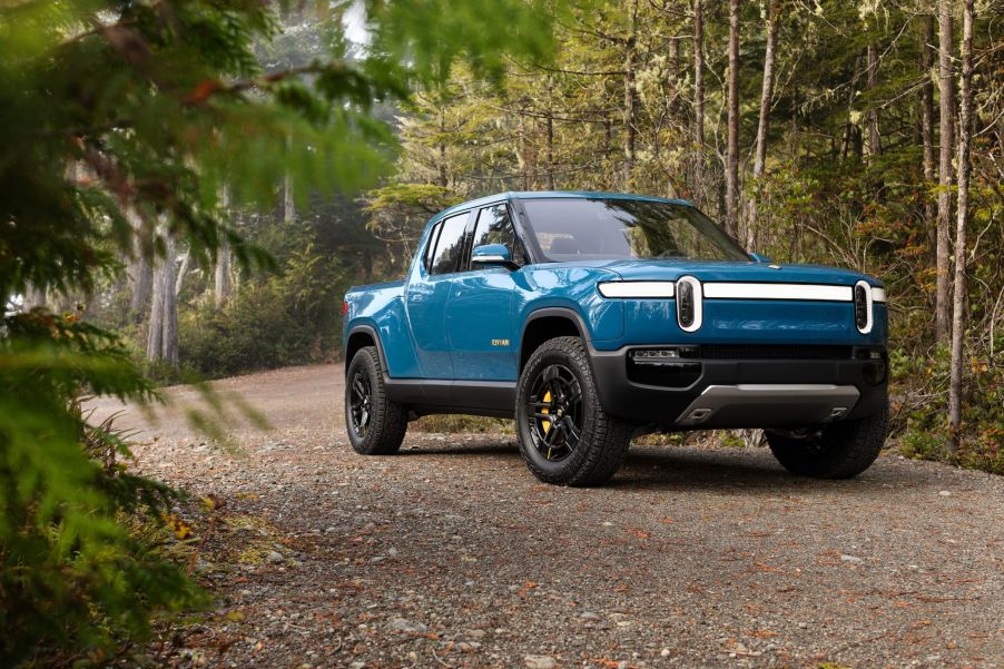 A blue Rivian R1T parked on a gravel road in a forest