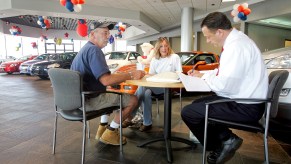 A couple sitting across from a car salesman while shopping for a car.