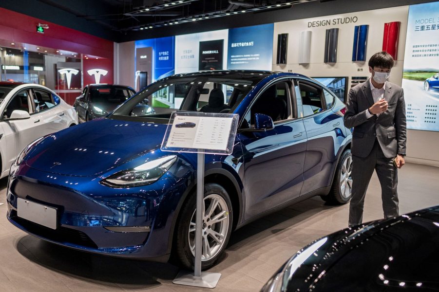 A vendor stands next to a blue Tesla Model 3 car on display at a shopping mall in Beijing